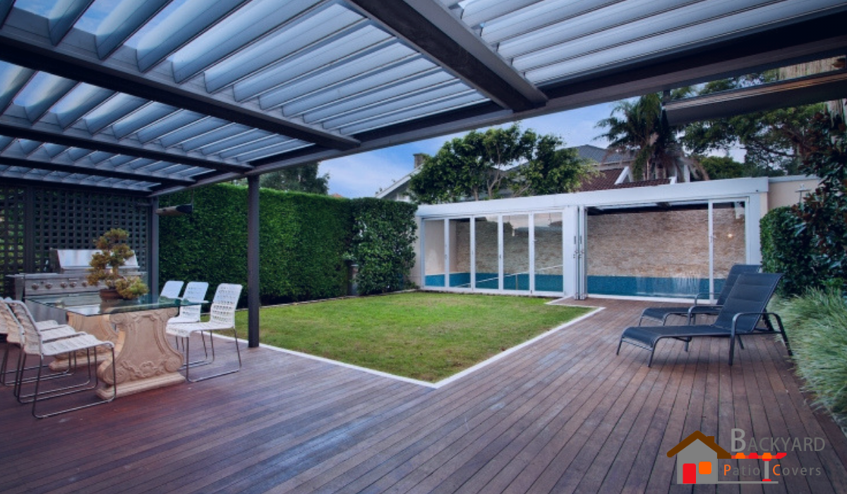 Custom aluminum louvered patio cover shading an outdoor dining area and wooden deck.