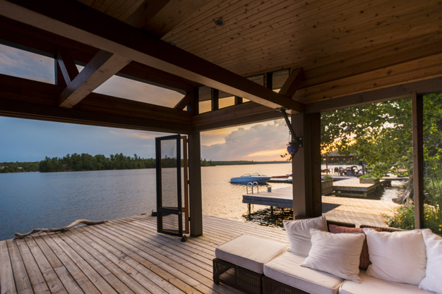 Covered outdoor patio with wood-beam ceiling, comfortable seating, and waterfront views