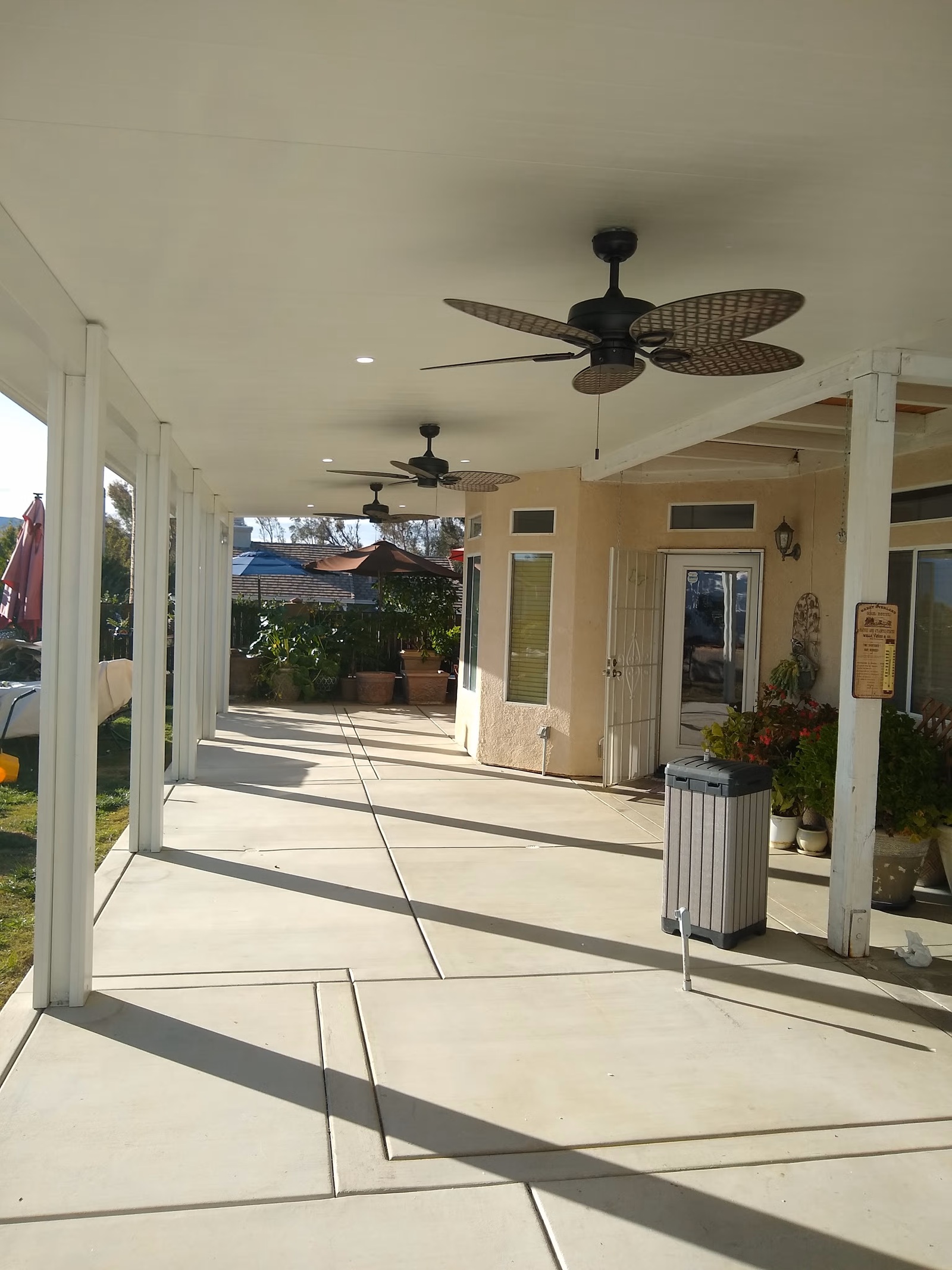 White patio cover with ceiling fans and recessed lighting providing shade over a spacious residential patio in Orange County