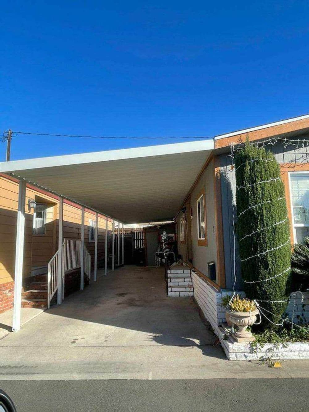 Carport in a residential area with clear sky, showcasing outdoor storage and landscaping.