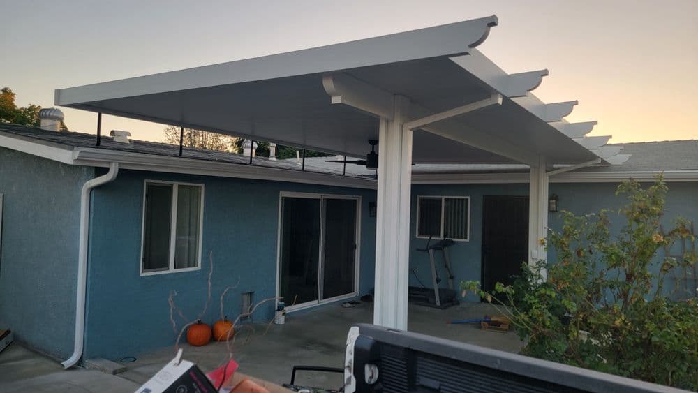 Modern backyard patio with a white awning and pumpkins, featuring gray siding and sliding doors.