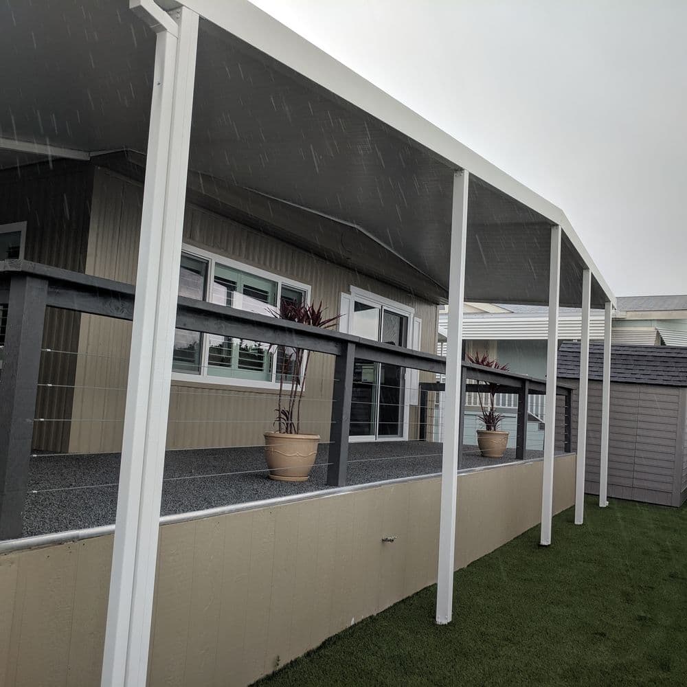 Porch with awning and railing, featuring potted plants, during rainy weather.