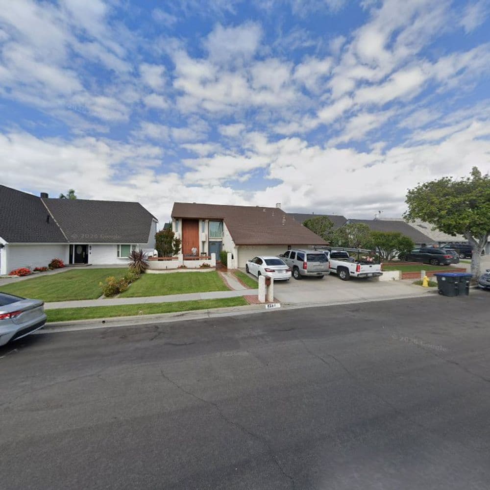 Residential neighborhood with two houses, parked cars, and clear blue sky.