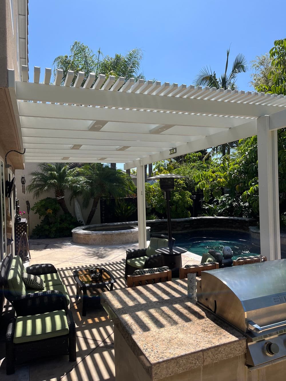 Elegant outdoor patio with a white pergola, grill, seating area, and swimming pool.