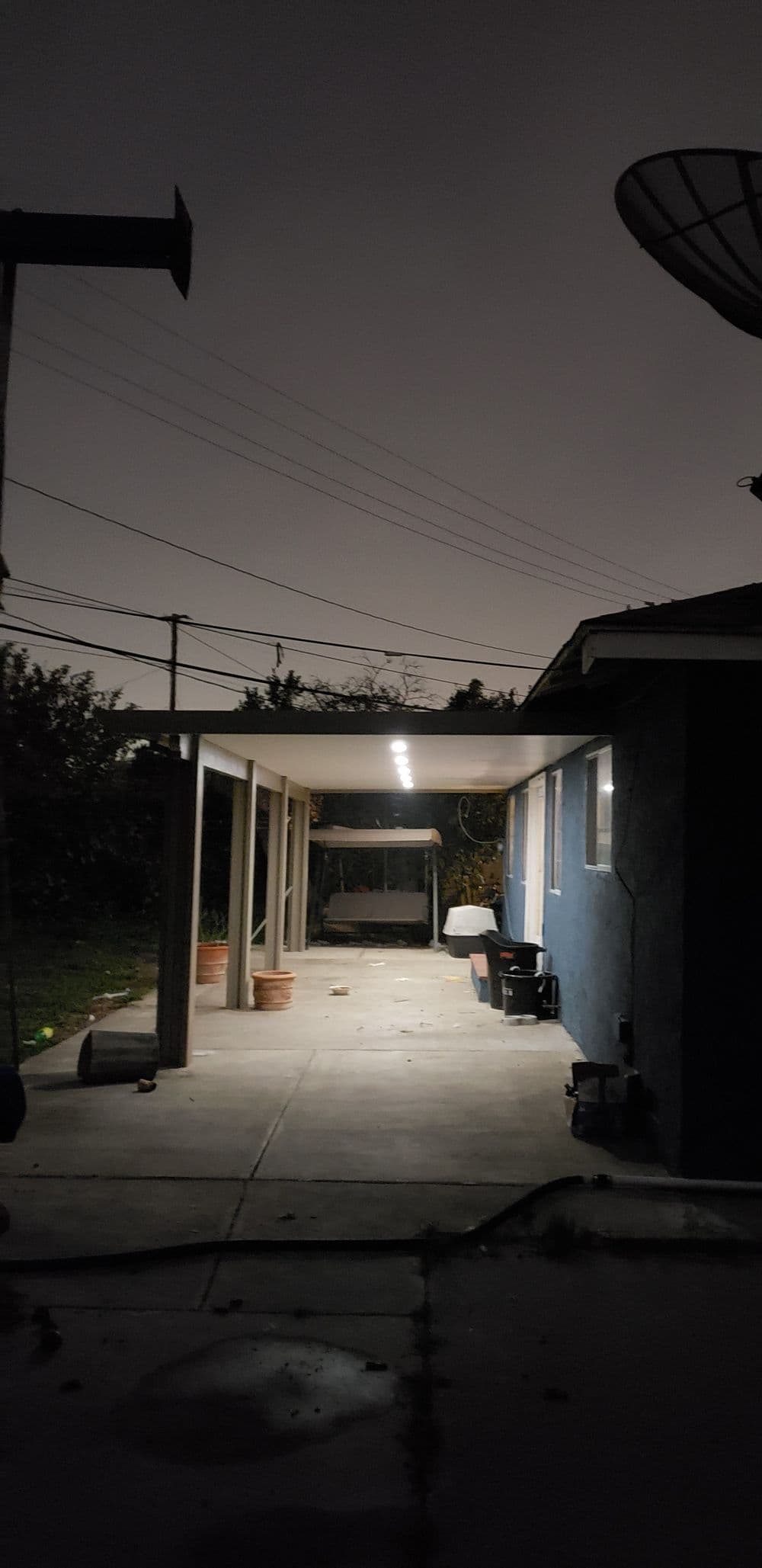 Dimly lit backyard at night featuring a covered patio and scattered potted plants.