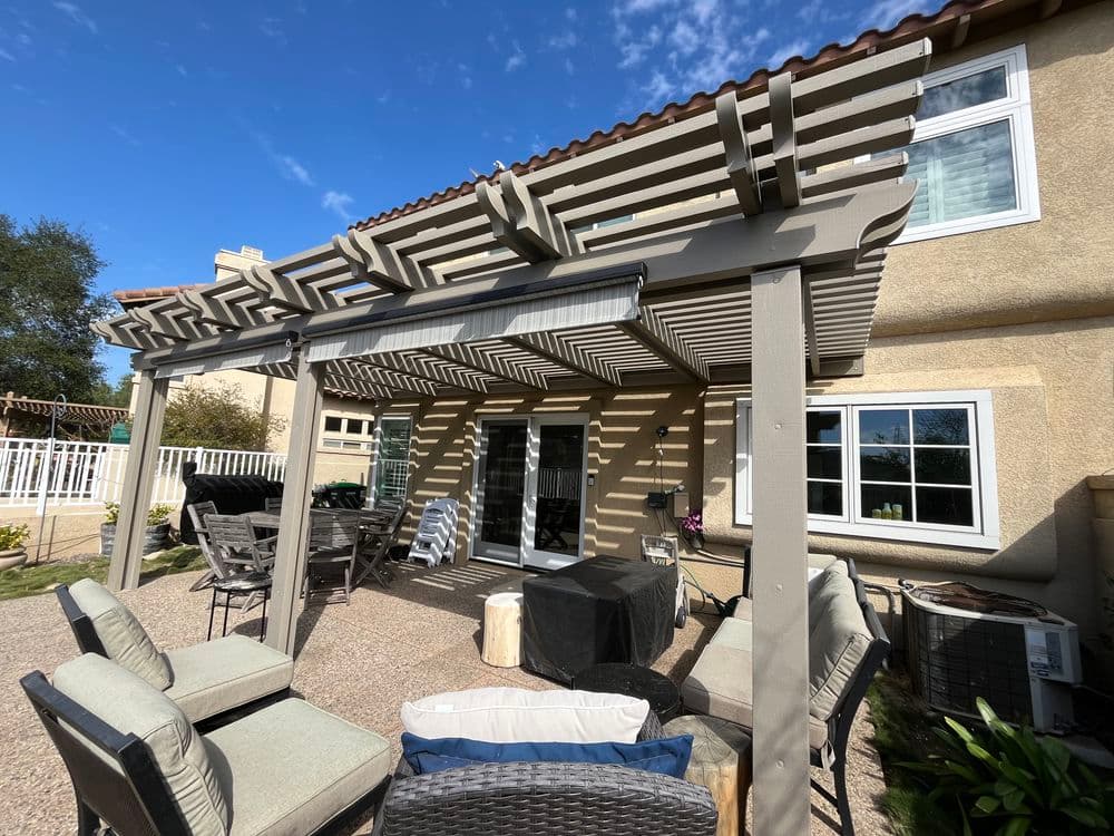 Modern patio with pergola, outdoor seating, and clear blue sky in residential backyard setting.