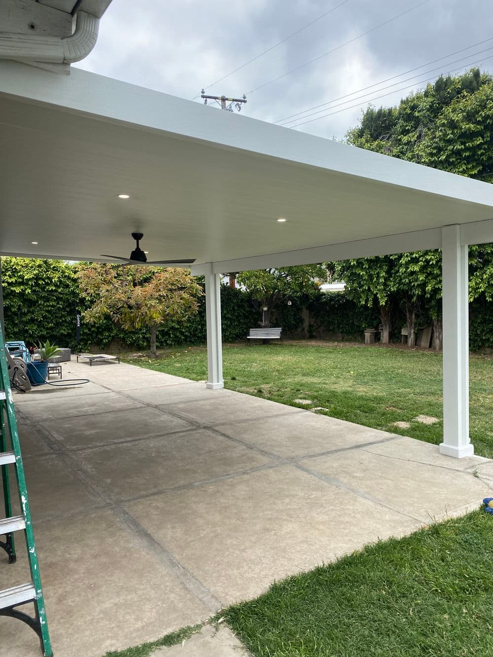 Patio cover with ceiling fan and recessed lights in a green backyard setting.