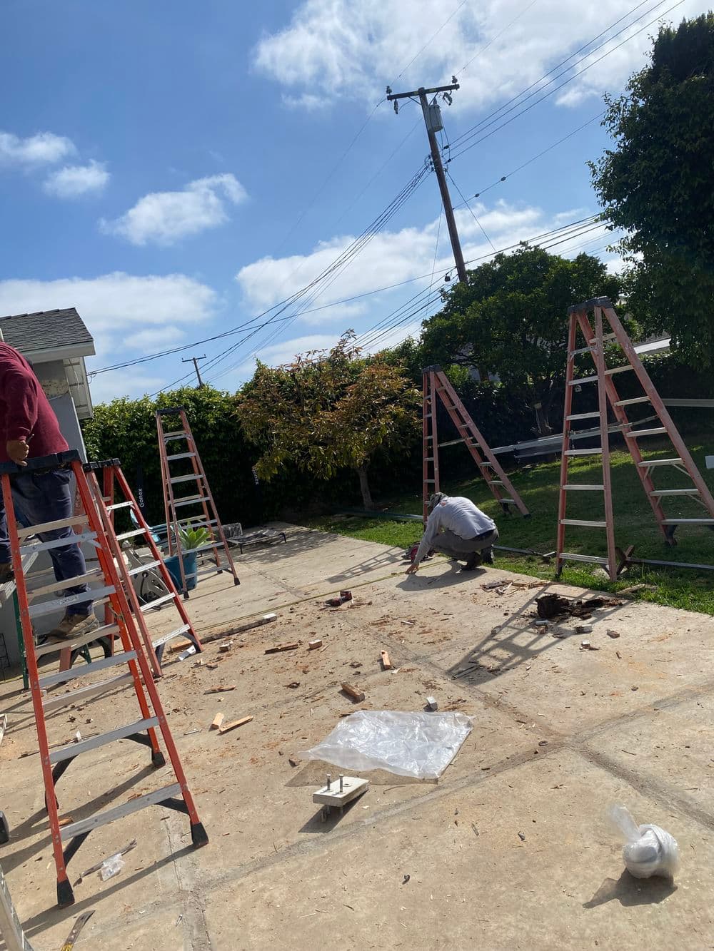 Construction workers using ladders in a backyard renovation project with scattered debris.