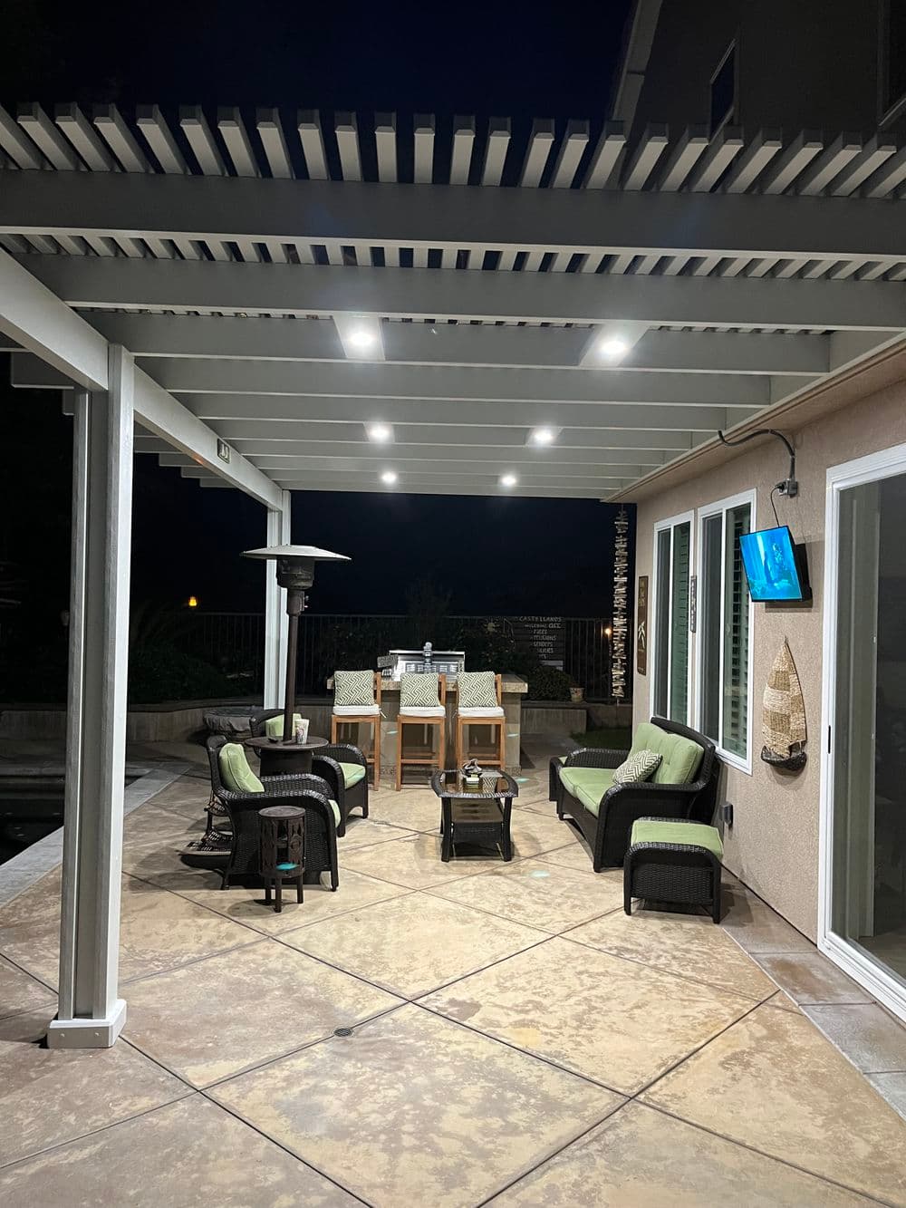Cozy patio with seating, heater, and outdoor dining under a pergola at night.