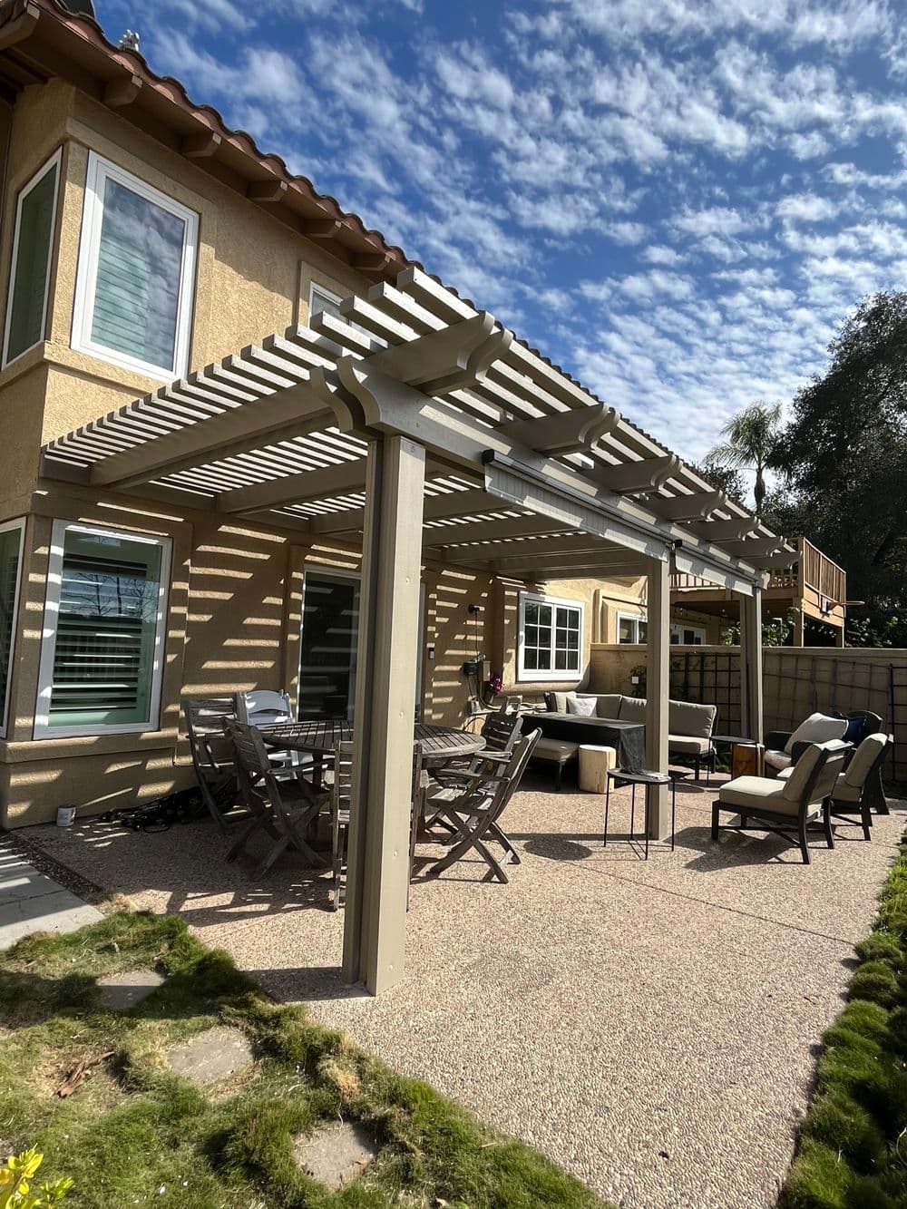 Outdoor patio with a pergola, seating, and a garden area under a blue sky.
