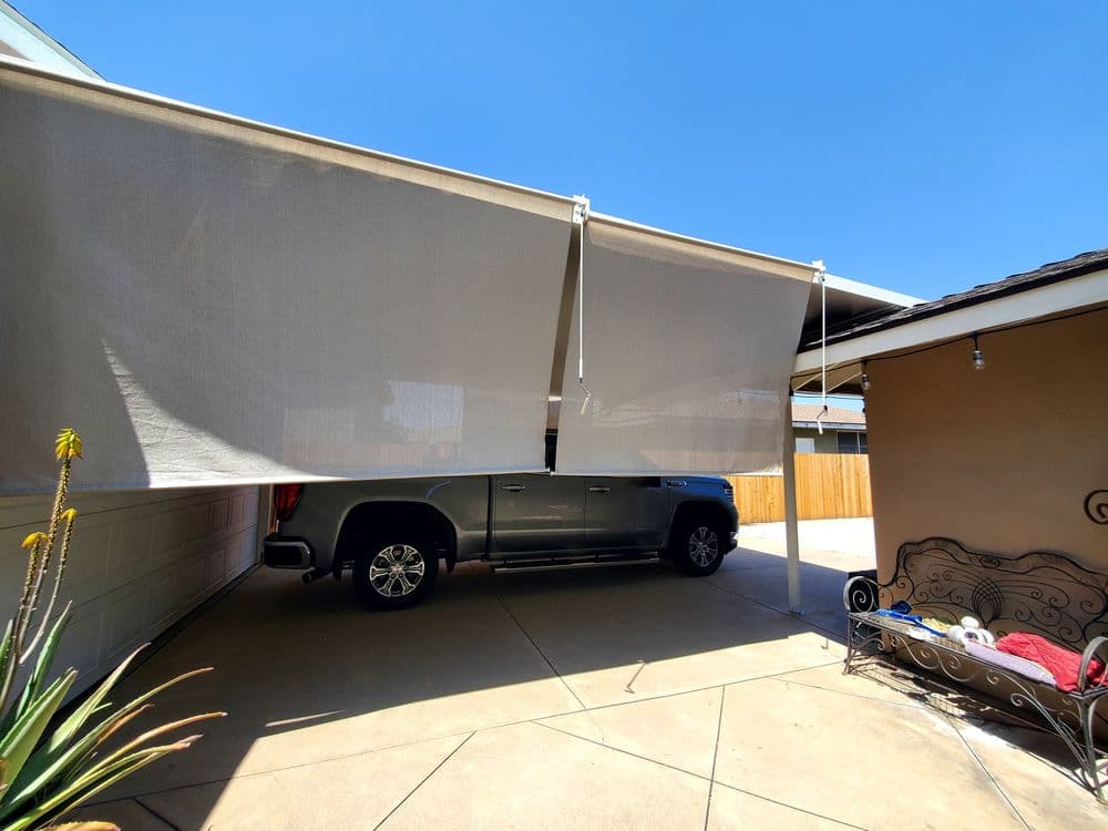 Retractable outdoor shades shielding parked truck in driveway under clear blue sky.