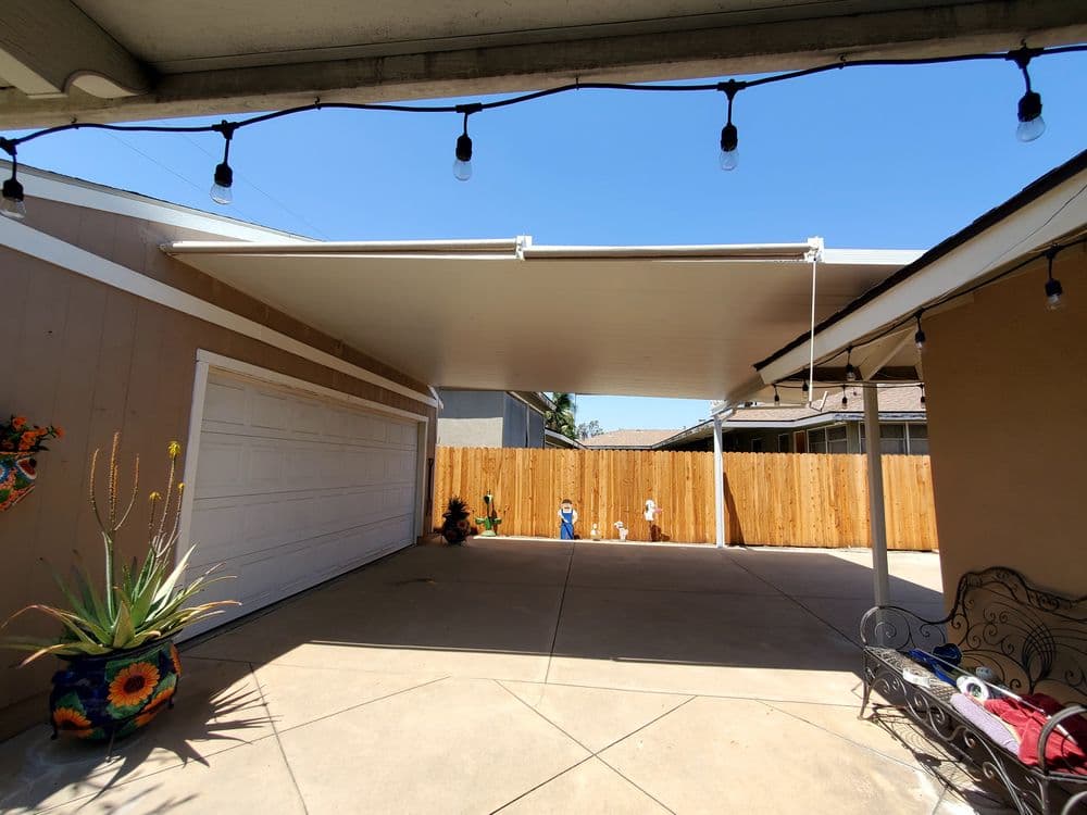 Carport with string lights, children playing outside, and wood fence in sunny backyard.