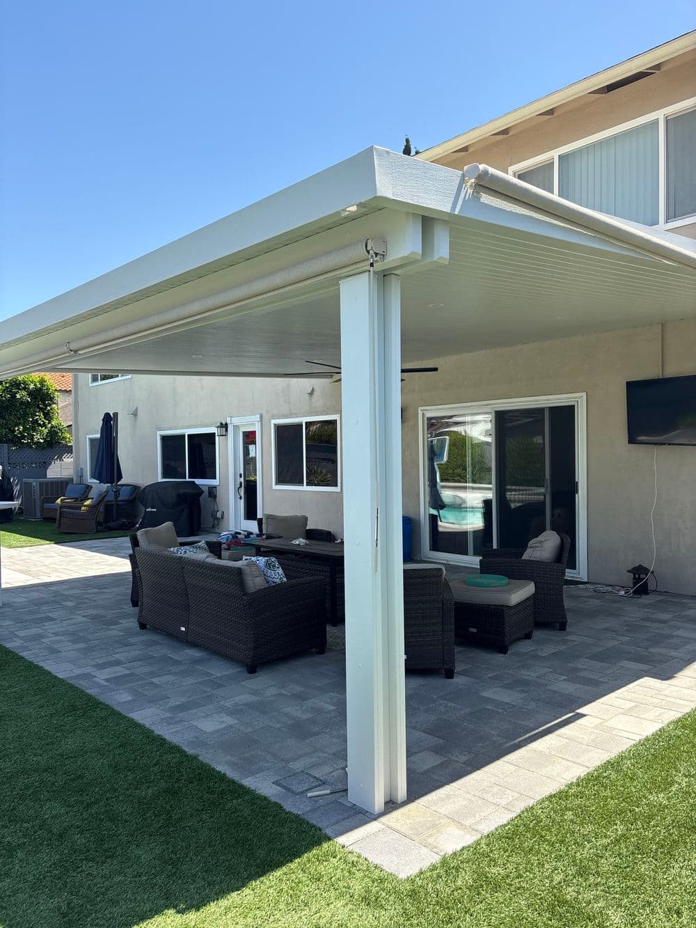 Modern backyard patio with shaded seating area, outdoor furniture, and green lawn.